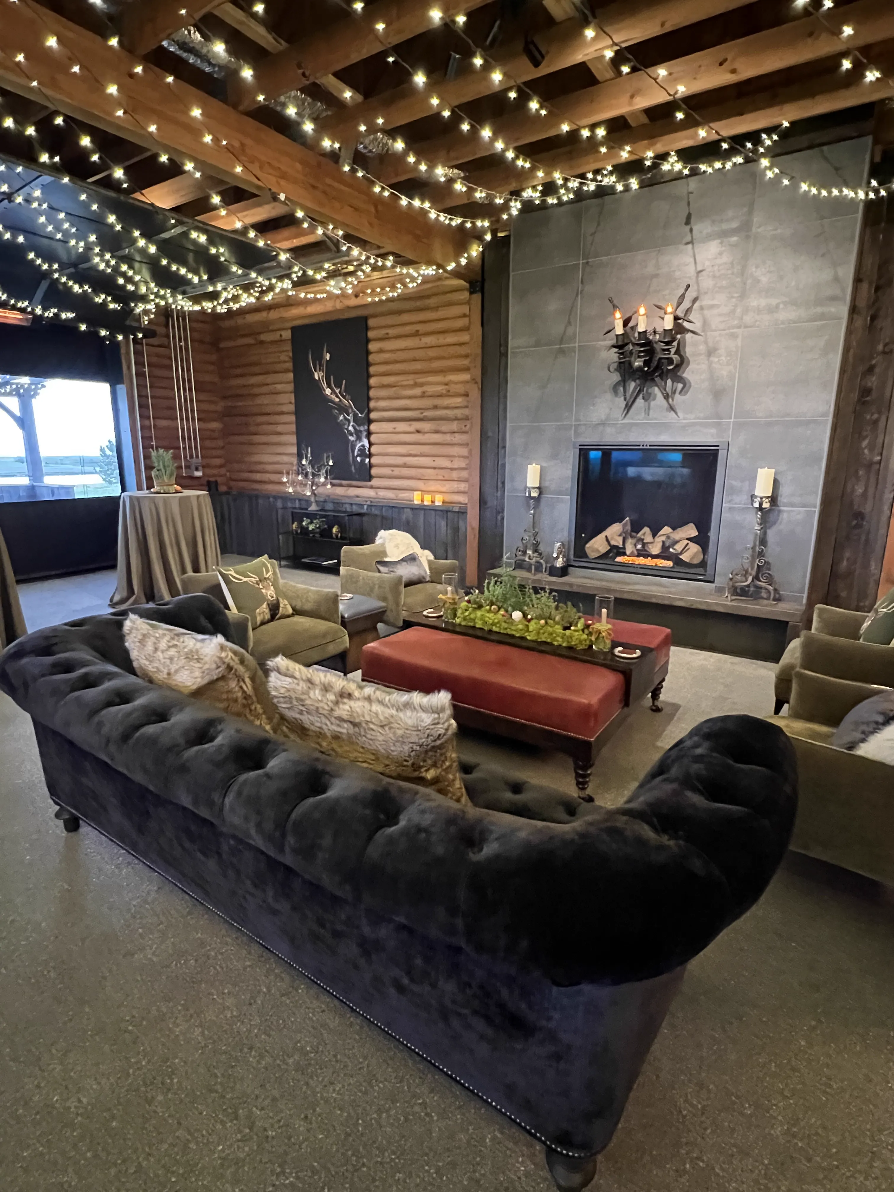 Rustic indoor lounge area in a log cabin with a fireplace and string lights