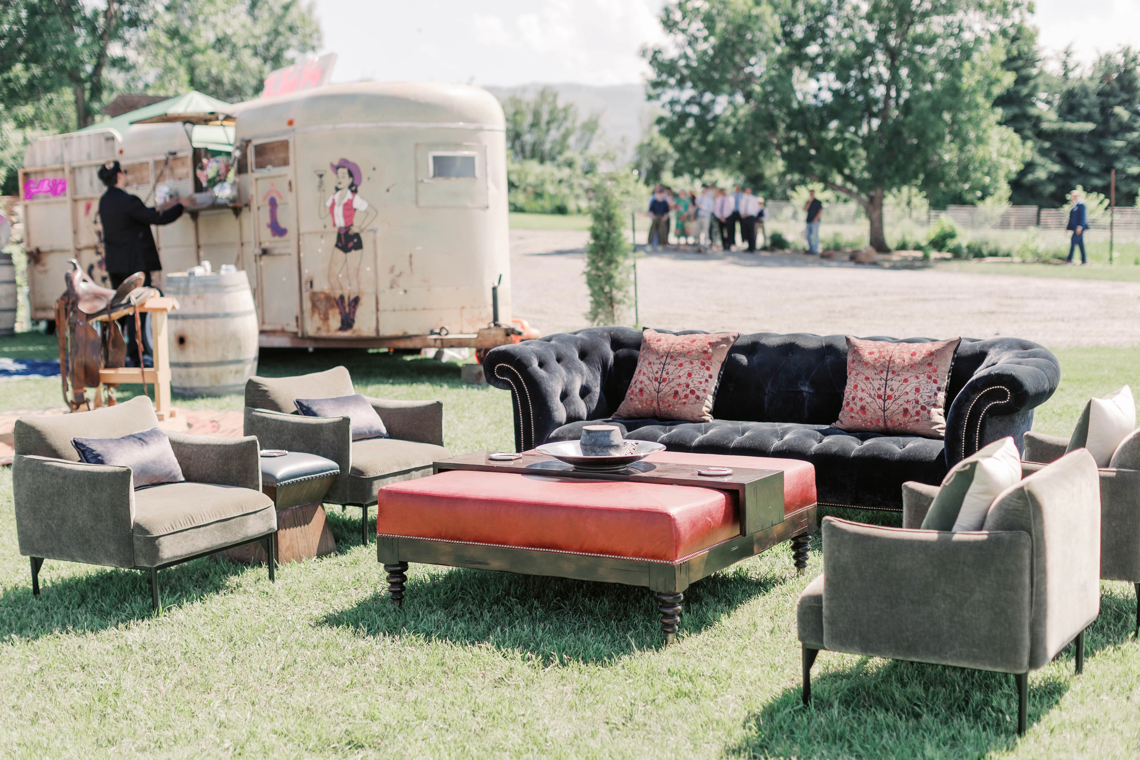 Sofas, armchairs, and a low table arranged on the lawn beside a vintage mobile bar.
